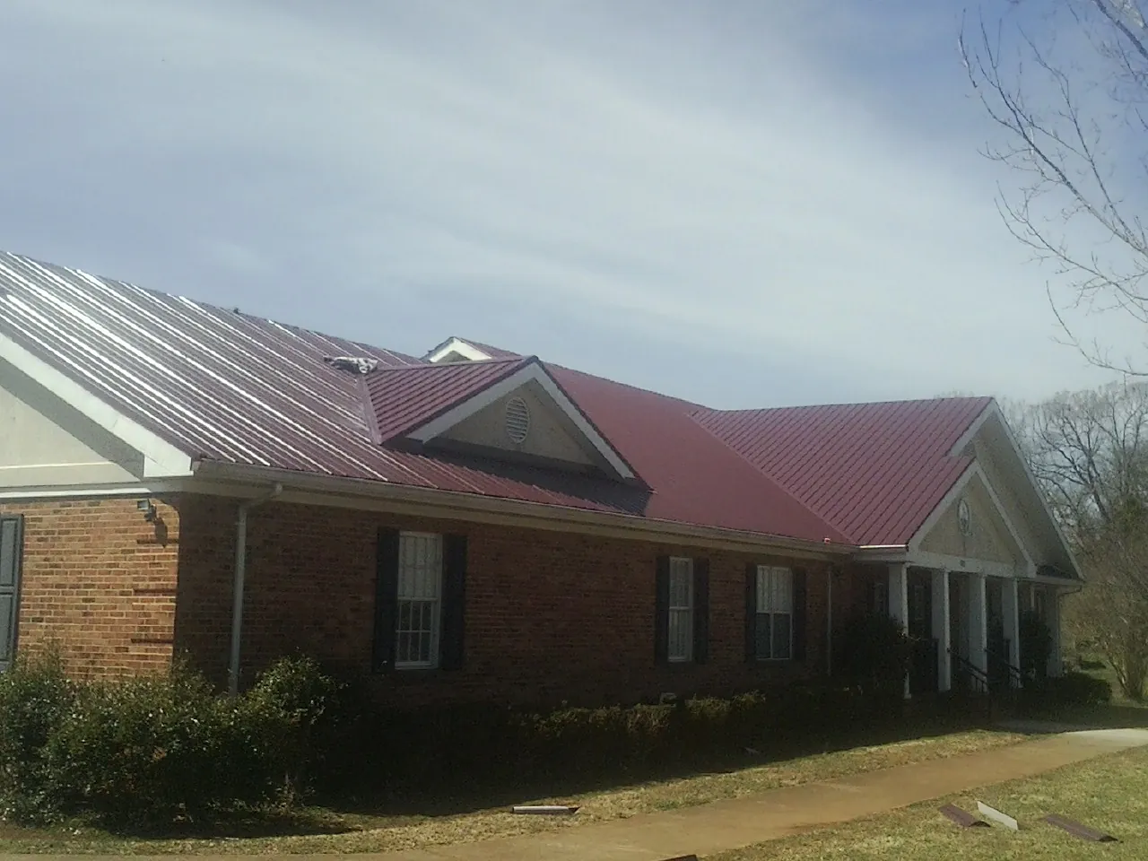 Red metal roof with gabled entries on a long brick building, from a Hail Damage Roof Repair job in Clearfield